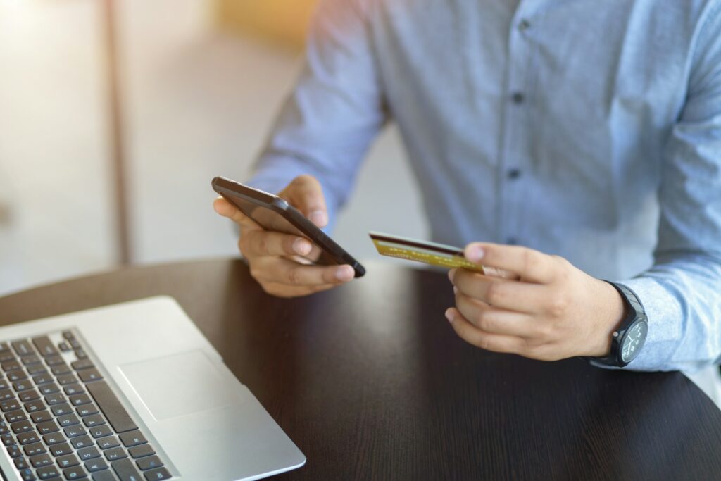 Person holding a credit card and phone near a laptop.